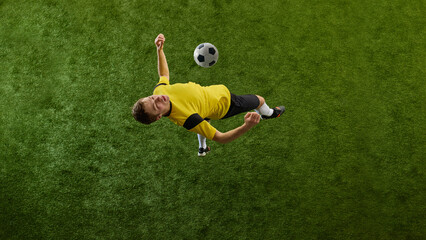 Top view dynamic image of determined young man, soccer player in motion on green stadium, kicking ball with chest, playing. Concept of sport, action, competition, game, active lifestyle. Ads © master1305