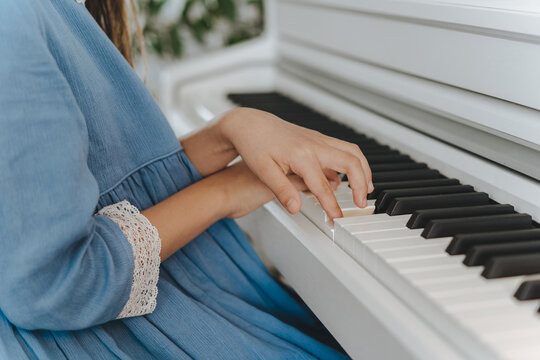 side view of a girl in a blue dress playing piano, hands close up