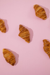 Fototapeta premium Vertical image of croissants scattered on a minimalist pastel pink background, puff pastry bakery piece