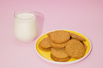 Whole wheat oatmeal cookies on a yellow plate with a glass of milk next to it on a pastel pink...