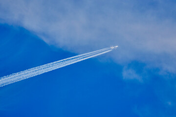 a plane climbing with tracks behind it in the blue sky