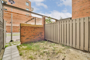 A contemporary outdoor area featuring a mix of brick and wooden structures, complemented by a small pathway and plant patches in a tranquil setting.