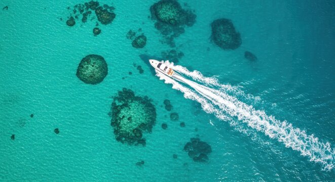 A close-up aerial view of a white speedboat cruising through crystal-clear turquoise waters leaving behind a white foamy trail