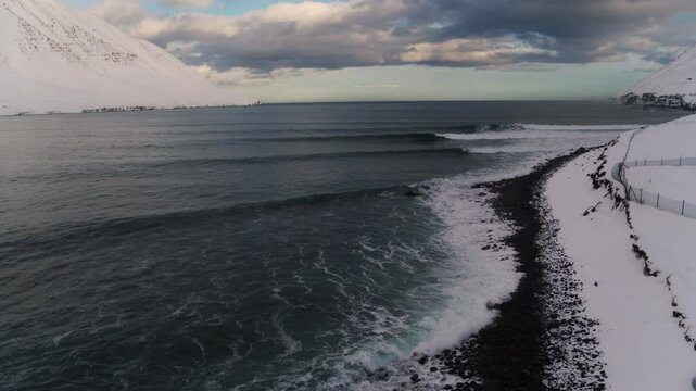 Drone perspective of Iceland winter coast where waves break against a snow covered shoreline