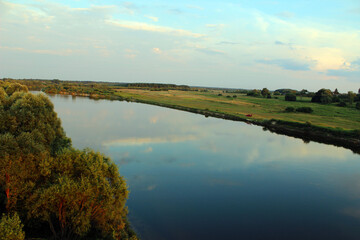 Serene river landscape under a clear sky with lush greenery and calm waters at golden hour in a rural area