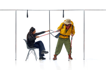 Hiker in yellow jacket struggling with businesswoman pulling trekking poles against white studio...