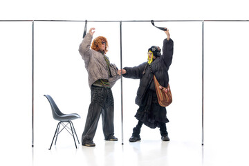 Gothic-dressed woman with oversized coat teasing curly-haired man in casual outfit against white...
