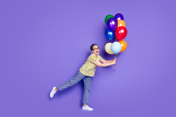 Fototapeta premium Cheerful elderly woman holding multi-colored balloons on a vibrant purple background