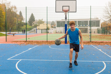 Man in sports clothes doing handling drills training at basketball playground court alone. Healthy lifestyle and outdoor sport concepts.  