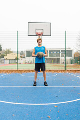 Fototapeta premium Low angle of an athletic man standing on basketball court with ball in his hands, waiting for the play and looking towards the camera. Healthy lifestyle and outdoor sport concepts. 