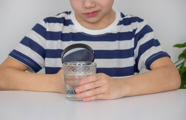 boy examines water in a glass with a magnifying glass. Selective focus