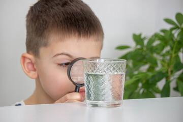 boy examines water in a glass with a magnifying glass. Selective focus