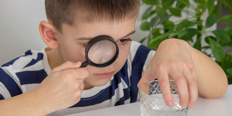 boy examines water in a glass with a magnifying glass. Selective focus