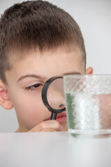 boy examines water in a glass with a magnifying glass. Selective focus