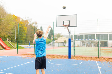 Young male basketball player playing basketball. Throwing the ball at playground. Precision shot. Unrecognizable young athlete playing basketball outside.