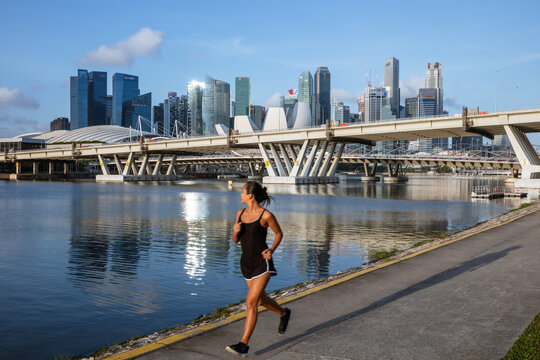 Young asian woman jogging in front of Marina Bay skyline, Singapore City