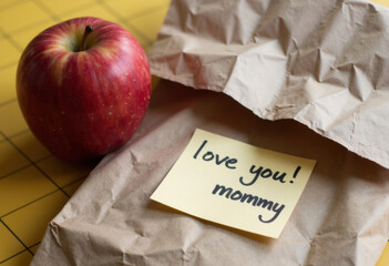 A red apple beside a note saying love you! mommy on crumpled paper