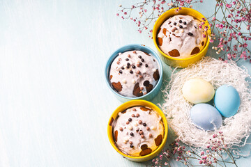Delicious Easter cupcakes and eggs on a light blue background with flowers. Easter cakes with glaze in bright baking molds of yellow and sky color. Copy space.
