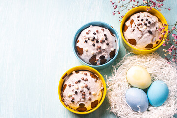 Delicious Easter cupcakes and eggs on a light blue background with flowers. Easter cakes with glaze in bright baking molds of yellow and sky color. Copy space.
