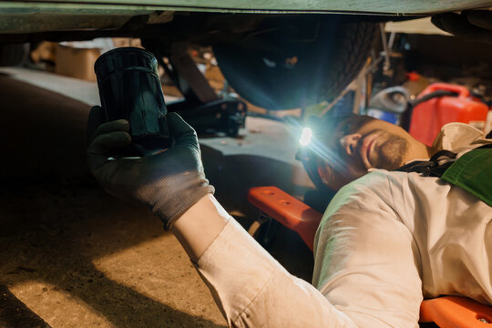 Mechanic wearing headlamp inspecting oil filter under vehicle in auto repair garage
