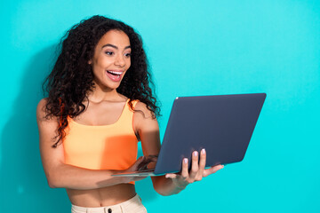 Smiling young woman using a laptop against teal background, expressing joy and excitement in a...