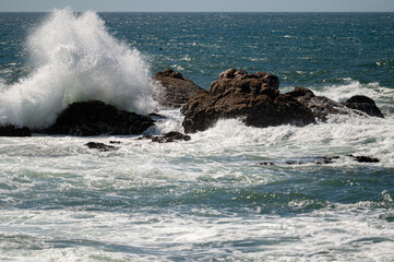 Fototapeta premium Waves crashing against rocky shoreline on a sunny day near the ocean