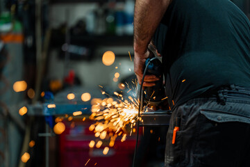 Dans un atelier de métallerie, gros plan sur les étincelles. Un homme qui est en train de couper...