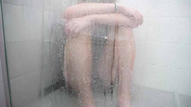 The man in the shower behind the glass. The silhouette of a man sitting in the shower behind a fogged glass with drops of water. The atmospheric image conveys a feeling of loneliness.
