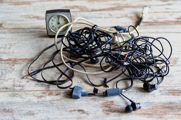 Old, dusty wires are tangled in a knot on a wooden background with a clock on a wooden table. Devices that have lost relevance, the era of wired technology.