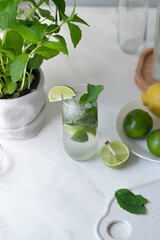 Glass with mojito cocktail drink on kitchen table, fresh summer green beverage with mint, lime and ice, home lifestyle interior