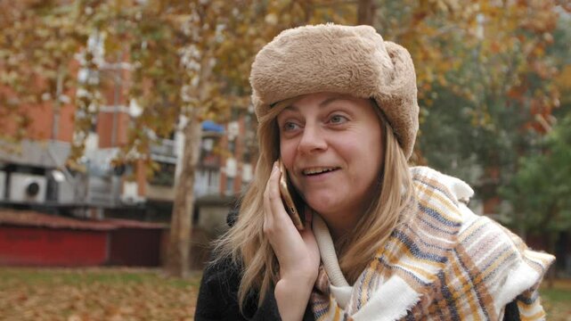 Woman wearing winter clothes talking on phone in autumn park