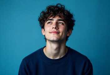 Fototapeta premium Thoughtful young man looking upwards on blue background.