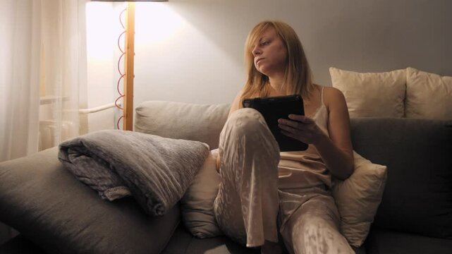 Woman relaxing on sofa with blanket and e-reader