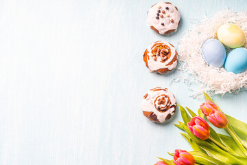 Easter cakes, painted eggs in the nest and tulips on a blue background. Copy space. Flat layout. View from above.