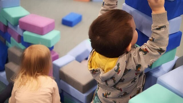 Playful toddlers stack colorful foam blocks, building tall towers in bright playroom. Playful toddlers develop motor skills and creativity through engaging play toddlers enjoy hands-on learning 