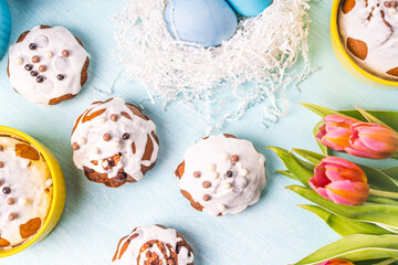 Easter cakes, painted eggs in the nest and tulips on a blue background. Copy space. Flat layout. View from above.