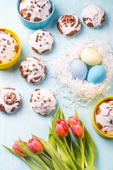 Easter cakes, painted eggs in the nest and tulips on a blue background. Copy space. Flat layout. View from above.
