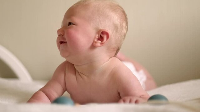 smiling infant baby lies on their tummy, looking up with bright eyes, Cild face expresses pure joy and curiosity, baby emotions, childhood happiness, home comfort