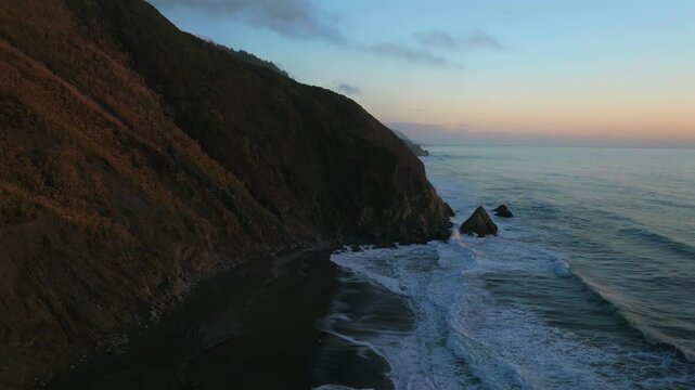 Northern California waves crashing bluffs cliffside mountain rocky rugged remote coastline aerial drone USAL Beach Campground sunset Sinkyone Wilderness sur swell black sand rocky shore static shot