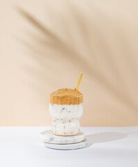 Korean whipped drink Dalgona coffee in a glass on a white beige background with morning shadow.