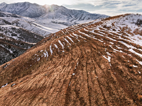 Trails on a Sun-scorched Hillside. A wintry evening landscape with a trails on a hillside, snow-capped mountains in the background - Powered by Adobe