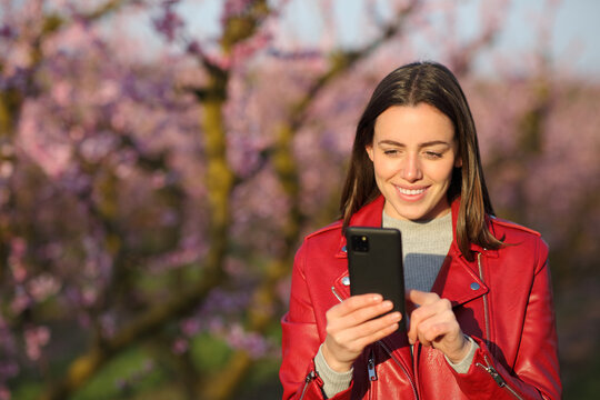 Front view of a happy woman in red using phone in a field