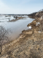 A vast and expansive body of water, which is completely surrounded by arid patches of dry grass and lush green trees in the vicinity, creating a beautiful natural landscape