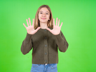beautiful teen girl wearing green sweater showing and pointing up with fingers number ten while...