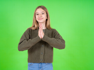 beautiful teen girl wearing green sweater praying with hands together asking for forgiveness smiling confident.