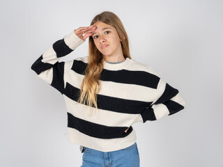 beautiful teen girl wearing striped sweater having problems, worried and stressed holds hand on forehead.
