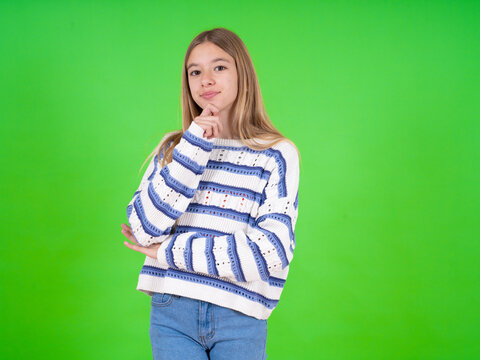 beautiful teen girl wearing striped sweater looking confident at the camera smiling with crossed arms and hand raised on chin. Thinking positive.