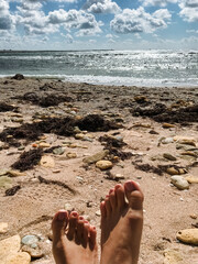 My bare feet are comfortably resting on a rocky beach beside the vast ocean, fully taking in the lovely and pleasant weather along with the breathtaking views of summer all around me