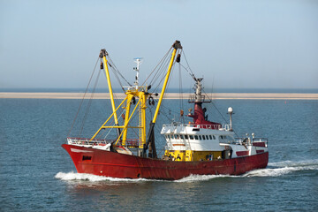 Red and yellow fishing boat at sea, in the background a sandbank