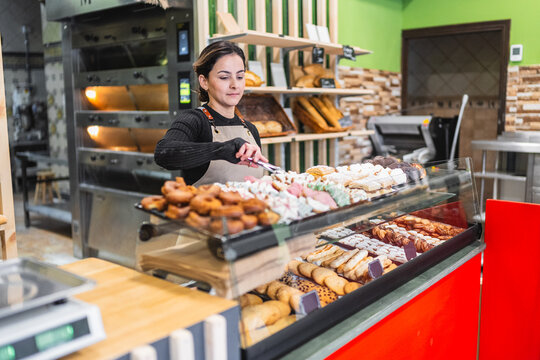 Baker arranging pastries in display case at bakery shop
